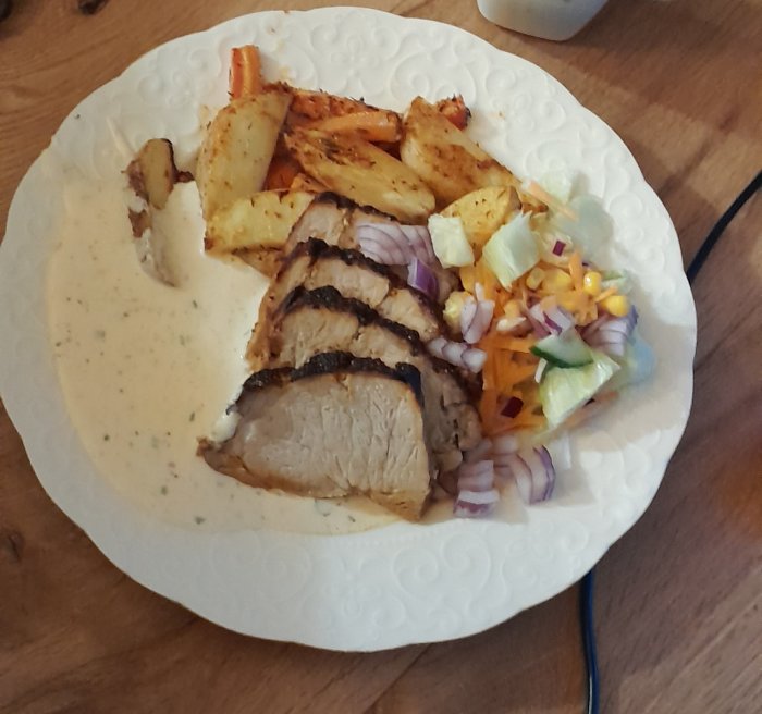 Tallrik med skivad grillad kött, klyftpotatis, sallad och sås.