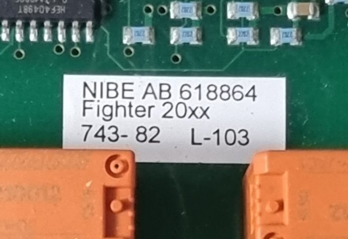 Etikett med text "NIBE AB 618864 Fighter 20xx" på elektronikkort, motståndsliknande komponenter, grönt kretskort, orange plastdetalj.