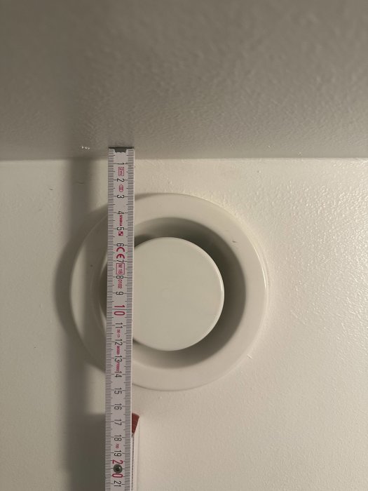 Måttband sträcks neråt mot golv, mäter avståndet från tak, nära vit downlight.