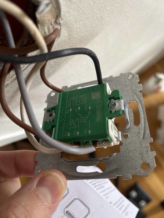 Hand håller eluttag med ledningar nära vägg under installation eller reparation.