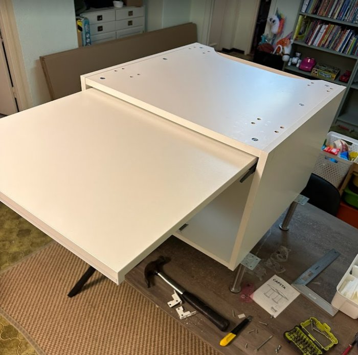 Ett vitt skrivbord under montering med verktyg och monteringsanvisning synliga på golvet.