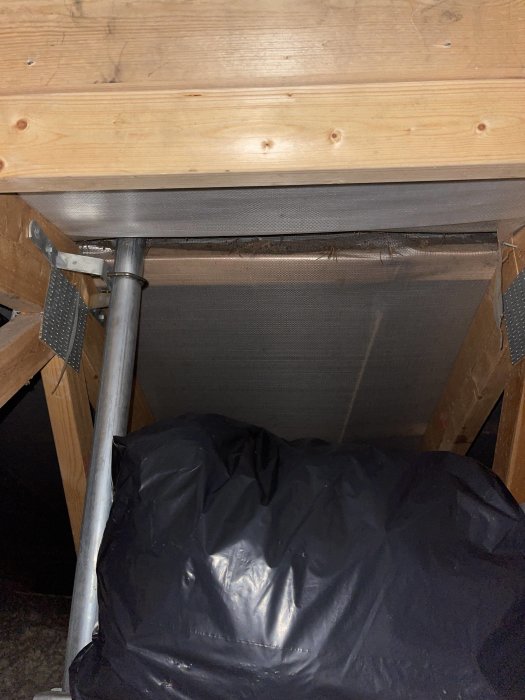 Under en säng med förvaringssystem, svart plast, träkonstruktion, metallelement, sängtillbehör, skymd vy.