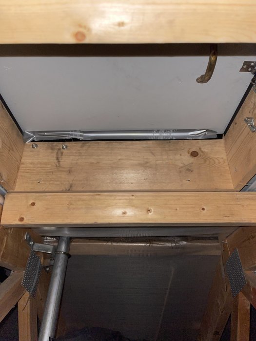 Undersida av ett träskrivbord med låda, metallhandtag, ledstänger och en metallfot synlig.