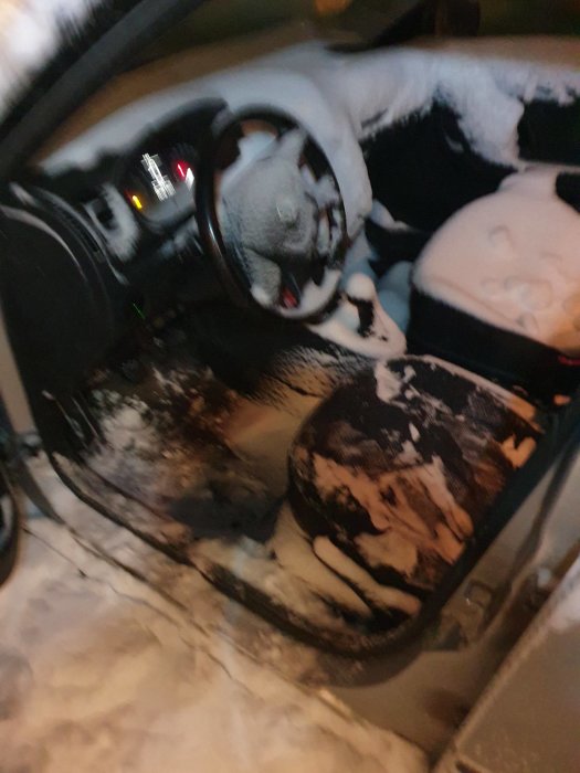 Bil interiör full med snö, öppen dörr, blurrig nattbild, kallt väder, vinter, förarsäte täckt av snö.