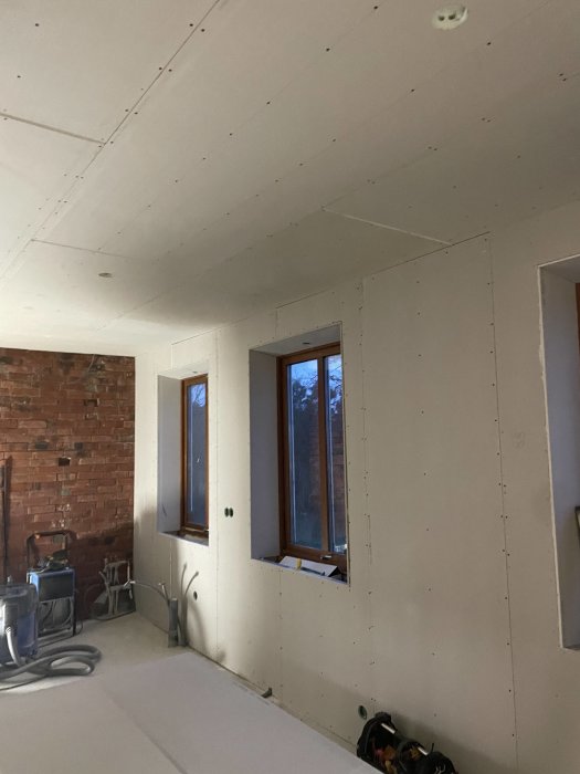 Ett rum under renovering med gipsskivor, exponerat tegel och arbetsmaterial.
