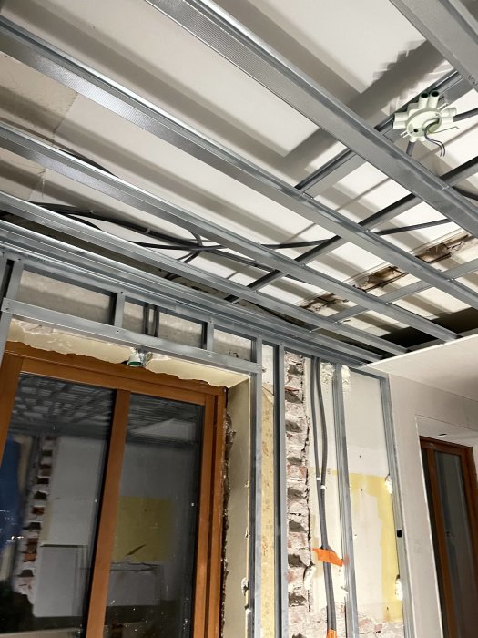 Renoveringsarbete på gång, metallstomme för gipsvägg, elinstallation, exponerat tegel, byggarbetsplats.