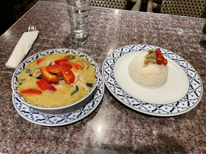 Ett bord med thai curry och ångkokt ris serverat på separata tallrikar. Glas vatten, servett och bestick syns också.