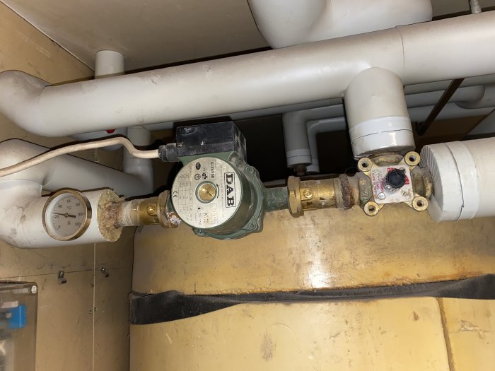 Vattenmätare och rörkopplingar i ett utrymme, några rör verkar ha korrosion.