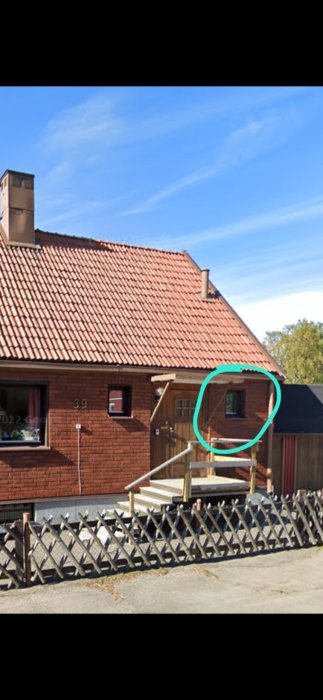 Ett tegelhus med takpannor, träveranda, och fönster markerat med en grön cirkel.