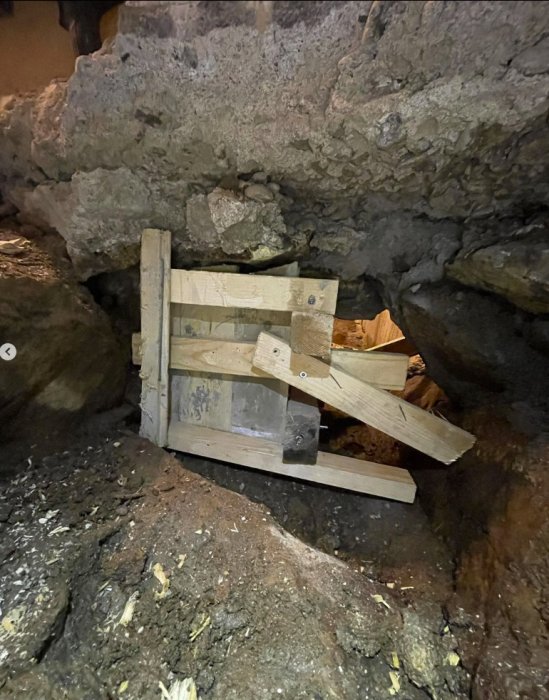 Trästöd stabiliserar stora stenblock i en grotta eller underjordisk miljö.