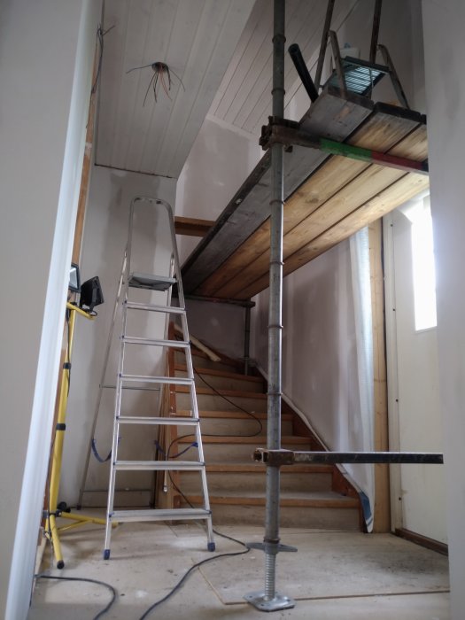 Renoveringsarbete pågår inuti ett hus med stegar, byggställning och osäkra elledningar synliga.