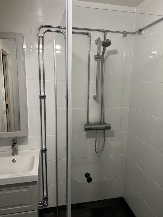 Modernt badrum med vit kakel, duschhörn, glasdörrar, handfat och spegel.