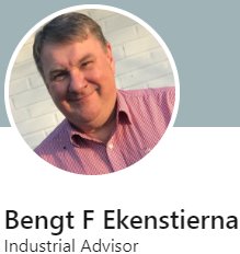 Man i rutig skjorta, leende, namntag, bakgrund oskarp, professionell miljö, industriell rådgivare.