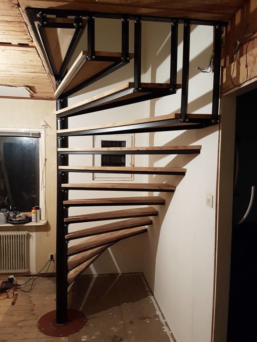 En spiraltrappa under konstruktion inne i ett rum med oskyddad vägg och synliga elledningar.