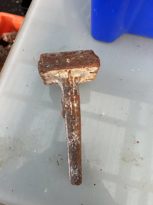 En rostig gammal hammare med trähandtag, ligger på ett suddigt gråblått underlag, möjligen en plastback.