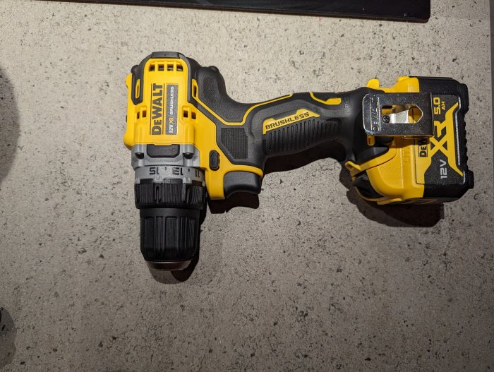 Gul och svart DeWalt borrmaskin liggande på grått underlag. Brushless motor, batteridriven, 12V.