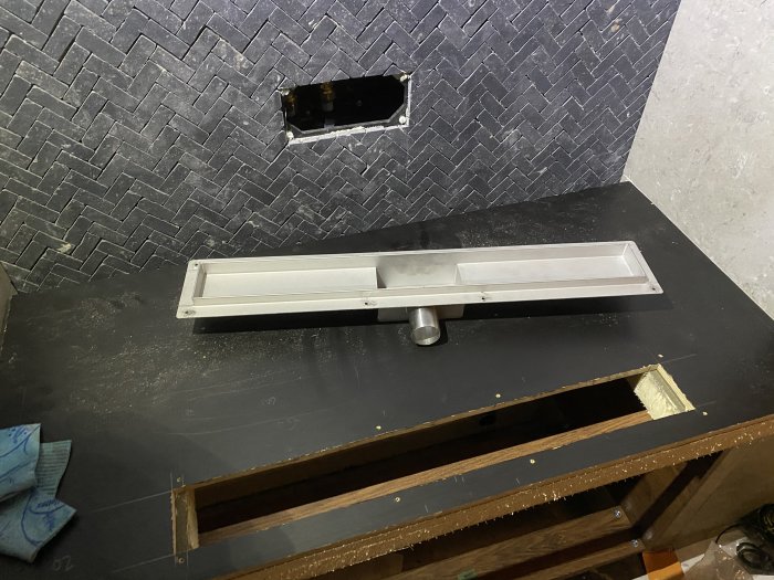 Renovering pågår, köksbänk med utskärning för diskho, svart bänkskiva, mörkt kakel, träkonstruktion synlig, dammigt.