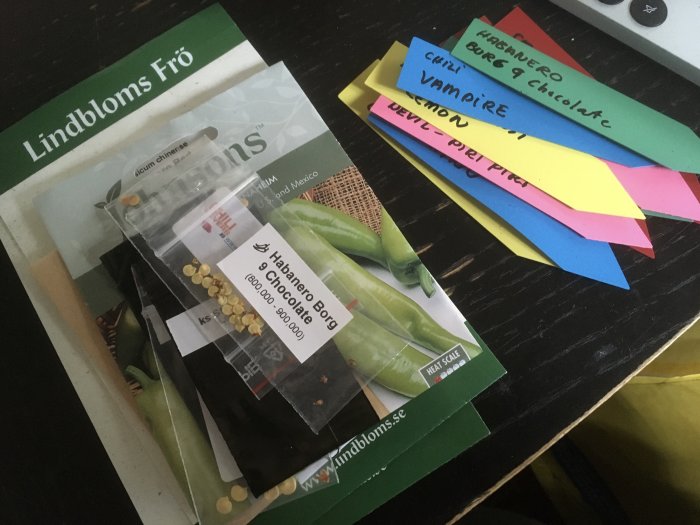 Flera fröpåsar, etiketter med text, träyta. Odling, trädgårdsarbete, planering.