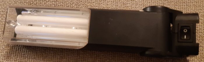 Batteriladdare med genomskinligt lock och fyra laddningsplatser på en beige matta.