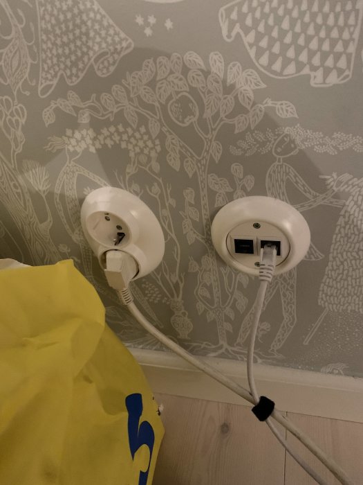 Elektriska uttag, kablar, vägg med dekorativt mönster, gult påsehorn i förgrunden.