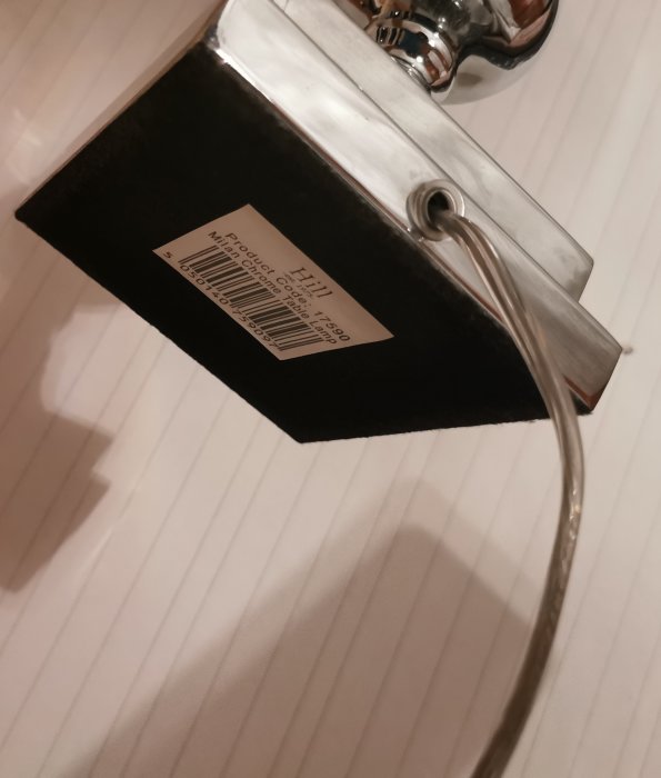 Bordlampa med svart skärm, silverfärgad arm och etikett på skärmen, fotograferad ovanifrån mot randig yta.