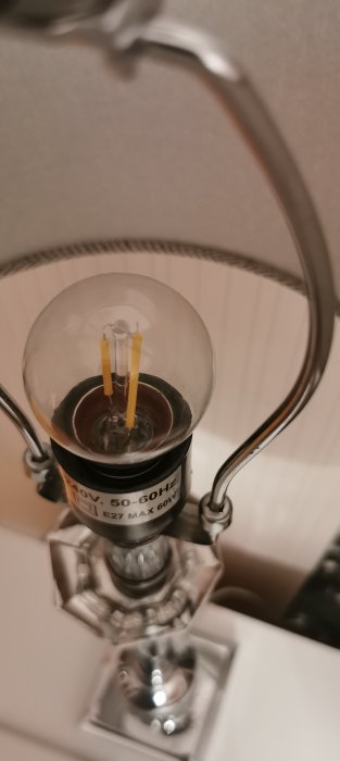 LED-lampa i fokus, monterad i silverfärgad armatur, märkt med spänning och sockeltyp, oskarp bakgrund.