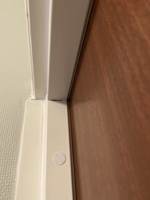 Vit dörrkarm, brunt dörrblad, väggdetaljer, möjlig golvlist och en liten vit plastdetalj/cirkel.