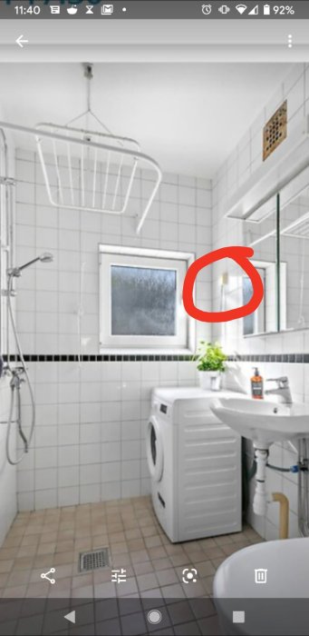 Modernt badrum med vita kakelväggar, dusch, tvättmaskin och handfat. Röd ring markerar något okänt.