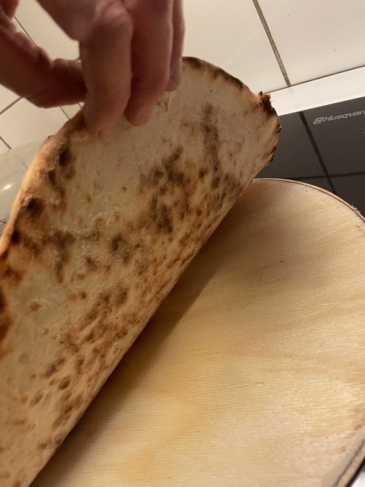 En person håller upp en nybakad, uppblåst pita eller naanbröd ovanför ett träskärbräda.