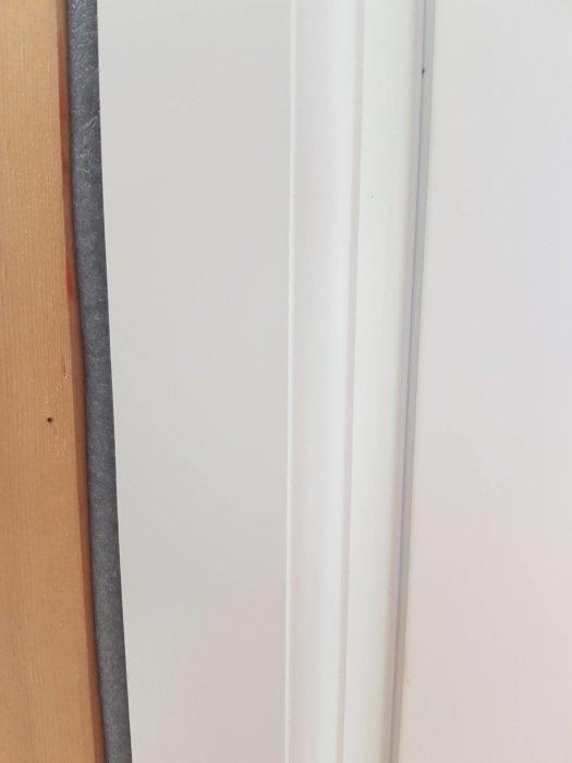 Detaljbild av en vit dörrkarm och en vägg med skuggning och texturkontraster.