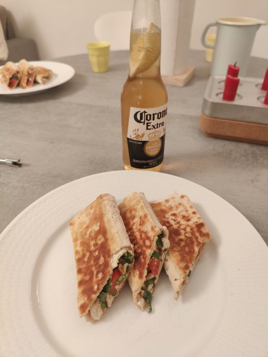 Ett snittat quesadilla på en tallrik med en Corona-öl, kondenspärlor på flaskan, inomhus matscen.