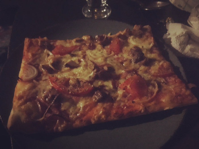 En pizza på en svart tallrik, mörk bakgrund, ser ut att vara kvällstid eller inomhus.