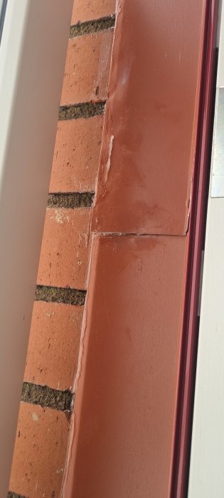 Ett närbildsfoto av en tegelvägg med en brunmålad karm eller pelare till vänster.