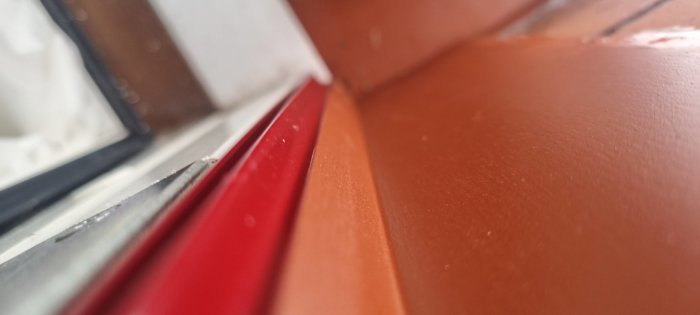 Närbild på en brun yta och röd kant vid ett fönster, defokuserad bakgrund, inomhus och dagsljus.