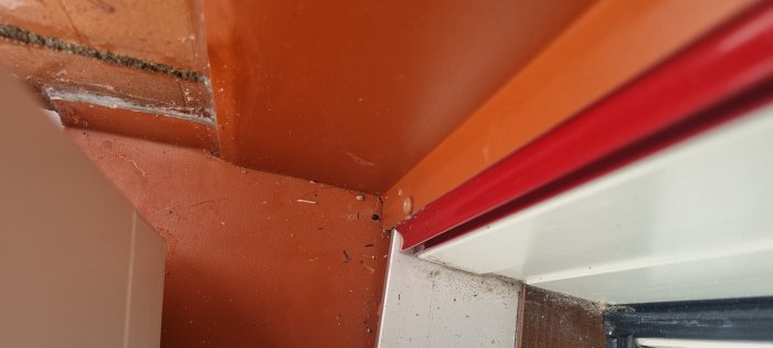 Inomhus hörn med orange väggar, röda balkar, vit list och byggdamm.