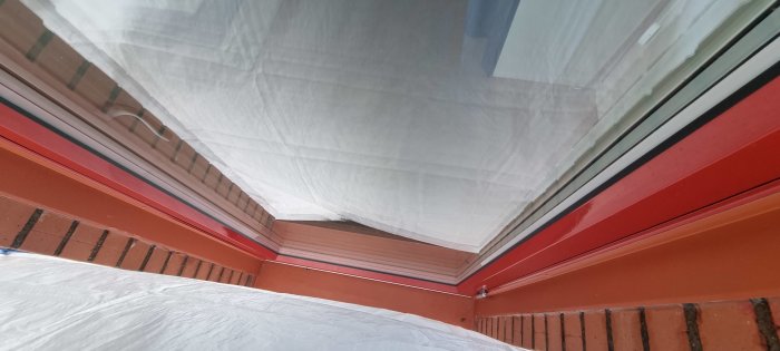 Utsikt under vit presenning, röda och grå strukturer, ovanlig vinkel, tegelvägg, delvis suddigt, dagsljus.