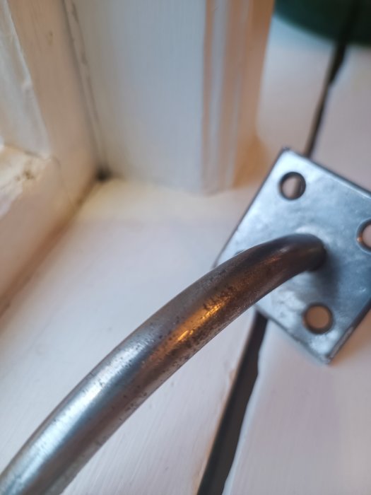 Metallhandtag med fäste, närbild, suddig bakgrund, inomhus, möjliga spår av användning.