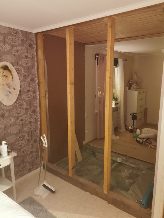 Interiör under renovering med träreglar, plastskydd på golvet och synliga verktyg.