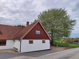 Traditionellt rött hus med vita knutar, träd, molnig himmel, utanför stadsområde, vägkant, lugn atmosfär.