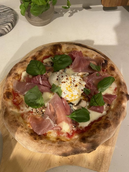 En pizza med prosciutto, mozzarella, basilika, svamp och ägg på träbricka.