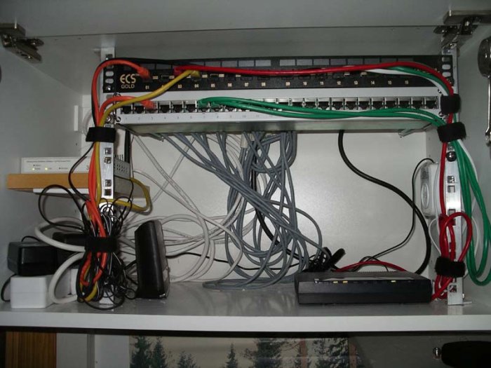 Nätverksskåp med patchpanel, switchar, rörigt kabelhanterings system, olika laddare och nätadaptrar.