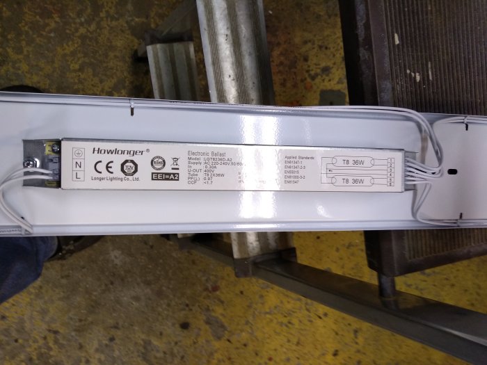 Fluorescentljusarmatur öppnad, elektroniskt driftdon synligt, installationsetiketter för T8 36W-rör, industriell bakgrund.