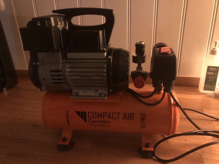 En kompakt luftkompressor med märkningen "COMPACT AIR OIL FREE" placerad på ett trägolv.