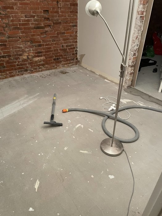Ett rum under renovering med synliga murtegelväggar, en dammsugare och en stående lampa.