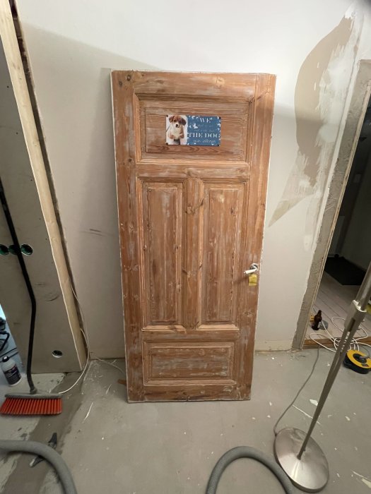 En gammal dörr står lutad mot en vägg i ett rum under renovering med redskap omkring.