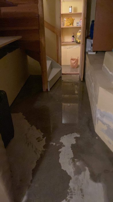 Ett källarutrymme med trappa och hyllor, drabbat av vattenskada och översvämning.