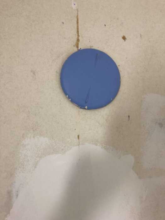 En blå cirkelformad föremål på en smutsig vägg med spricka och vattenfläckar.