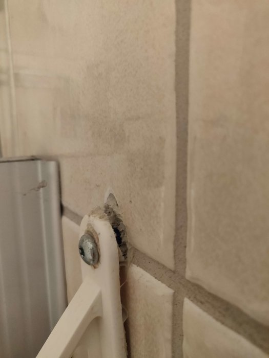 Vit värmeelement, fäste, kaklat badrumsvägg, nedsmutsning, installationsdetalj, närbild.