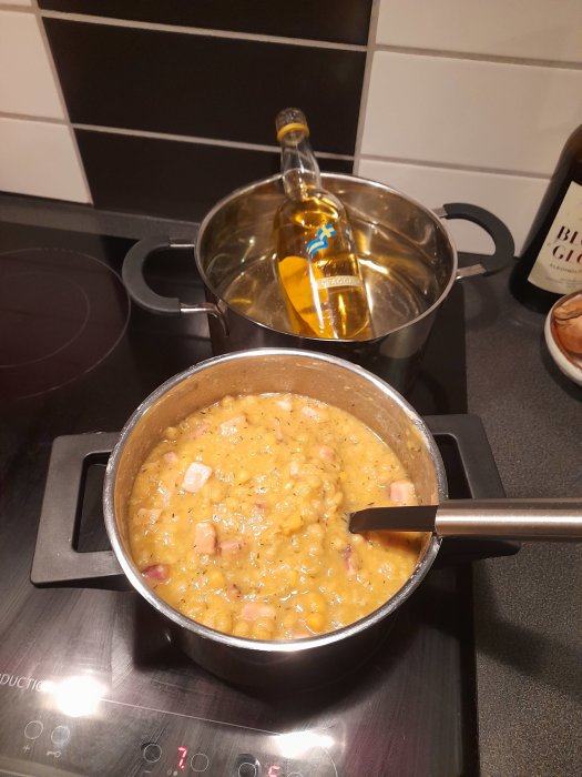 Matlagning på spis: gryta med gulasch eller ärtsoppa och en flaska på spishällen i kök.