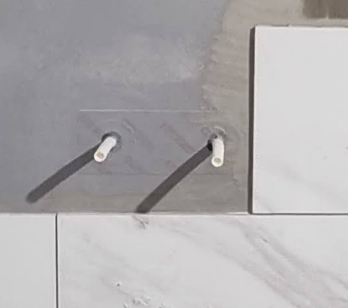 Två vita kablar stickandes ut från en grå och vit kaklad vägg.